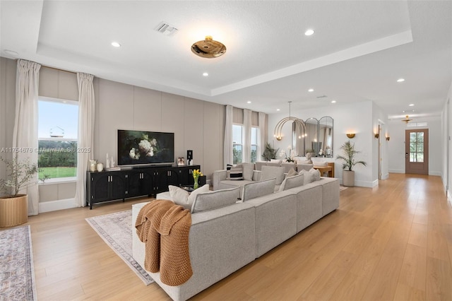 living area with light wood-type flooring, visible vents, a tray ceiling, and a wealth of natural light