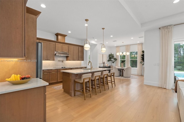 kitchen featuring a breakfast bar, black electric stovetop, decorative backsplash, a sink, and under cabinet range hood