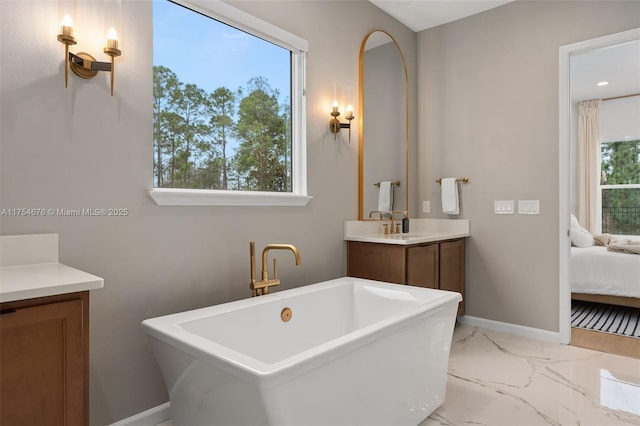 ensuite bathroom with baseboards, connected bathroom, marble finish floor, vanity, and a freestanding tub