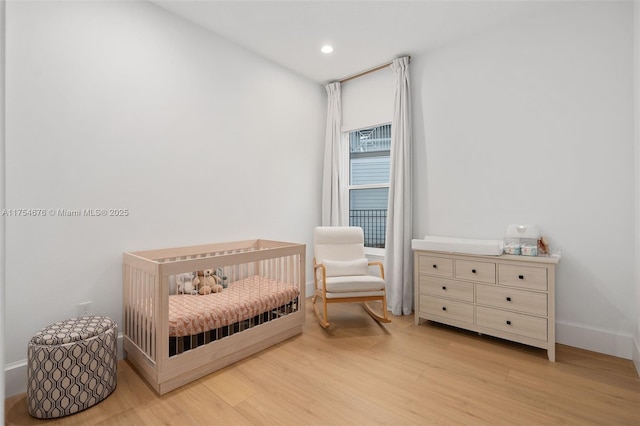 bedroom featuring a nursery area, baseboards, wood finished floors, and recessed lighting