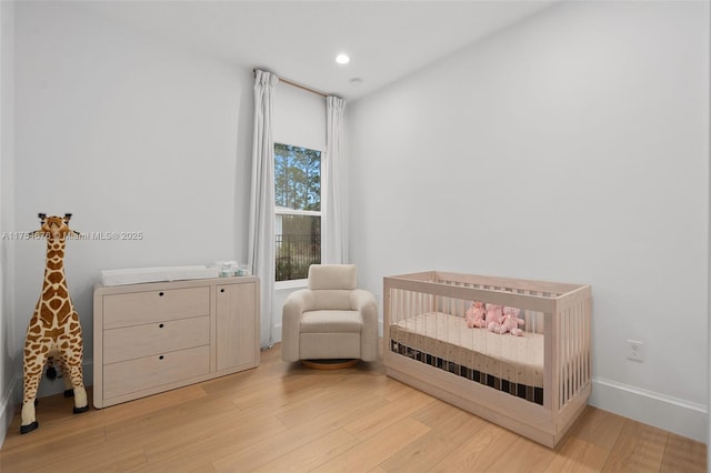 bedroom featuring a crib, light wood-style flooring, baseboards, and recessed lighting