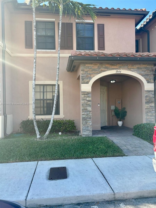 property entrance with stone siding, a tiled roof, and stucco siding