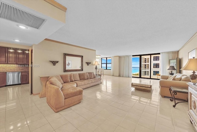 living area with light tile patterned floors, a textured ceiling, visible vents, and crown molding