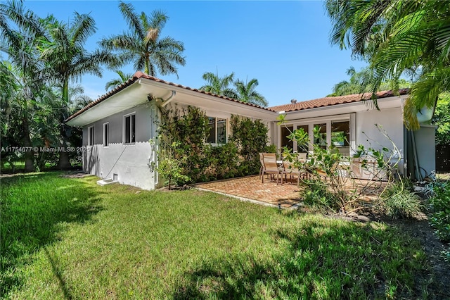 back of house with a tiled roof, a yard, a patio area, and stucco siding