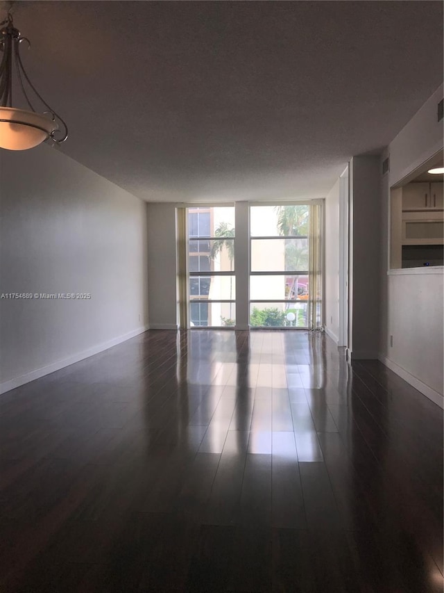 empty room featuring dark wood-style floors, baseboards, and a wall of windows