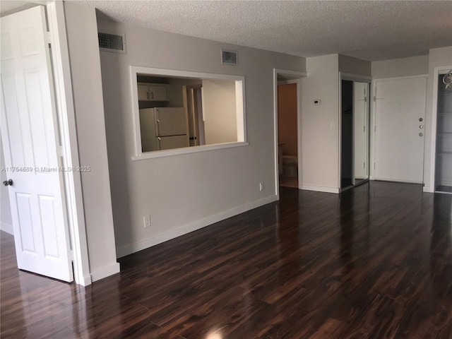 unfurnished room with dark wood-type flooring, visible vents, a textured ceiling, and baseboards