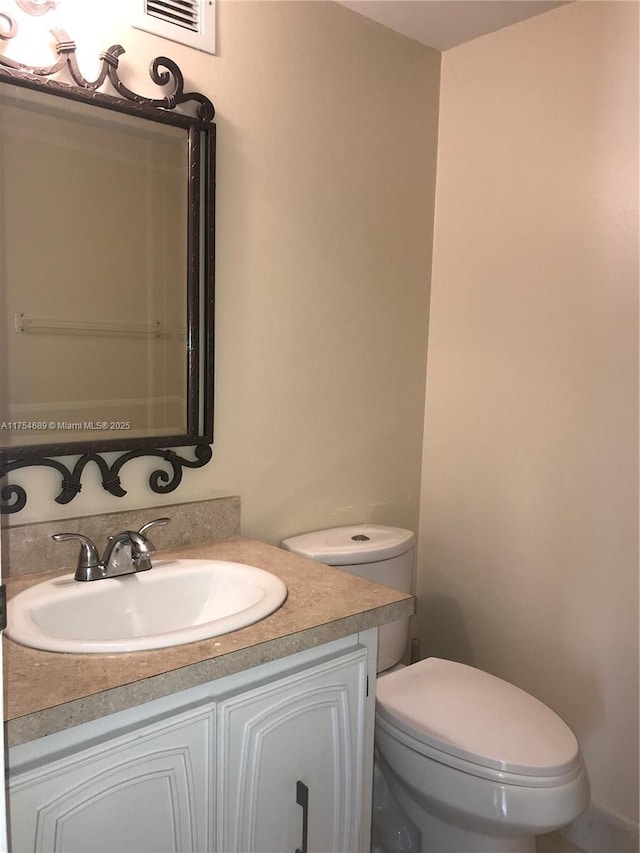 half bath with toilet, vanity, and visible vents