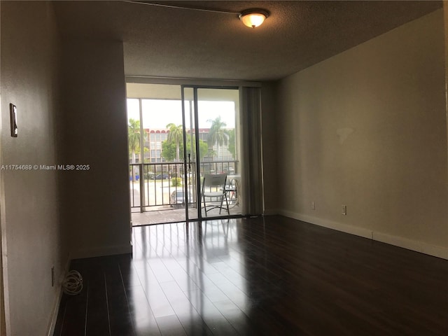 spare room featuring expansive windows, baseboards, dark wood-style flooring, and a textured ceiling