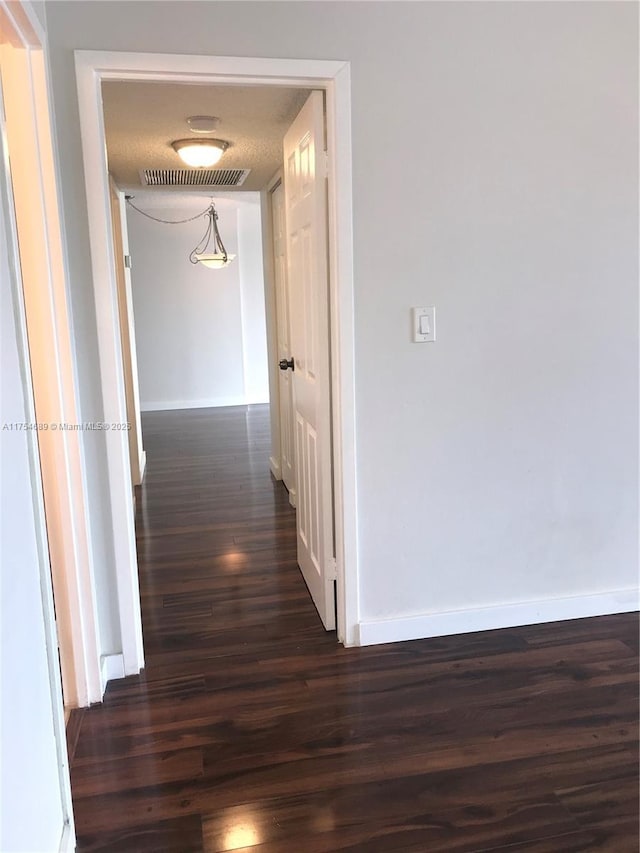 corridor featuring dark wood-type flooring, visible vents, and baseboards