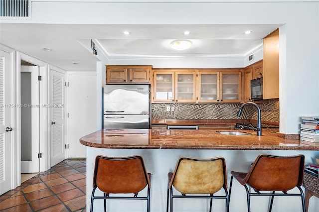 kitchen featuring tasteful backsplash, freestanding refrigerator, a sink, black microwave, and a peninsula