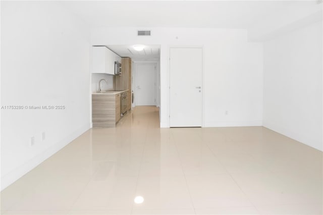 empty room with visible vents, a sink, baseboards, and light tile patterned flooring