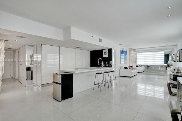 kitchen with light tile patterned floors, visible vents, open floor plan, a sink, and a kitchen bar