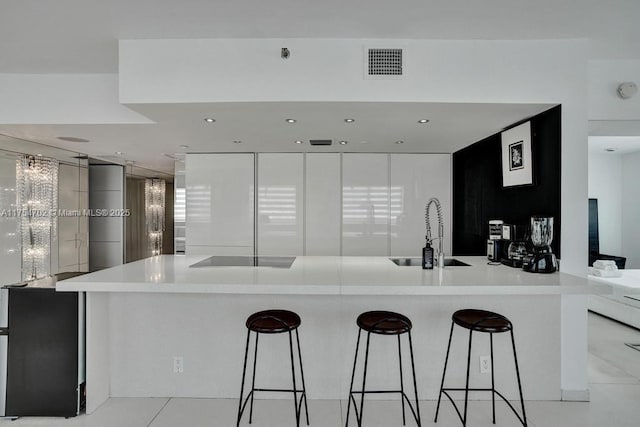 kitchen with black electric stovetop, a sink, visible vents, a kitchen breakfast bar, and modern cabinets