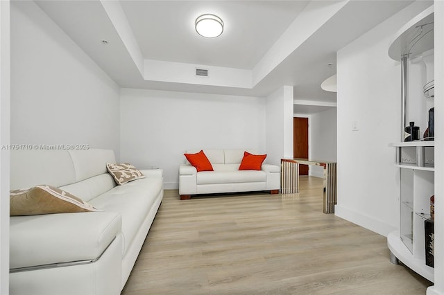 living room with a raised ceiling, visible vents, baseboards, and wood finished floors