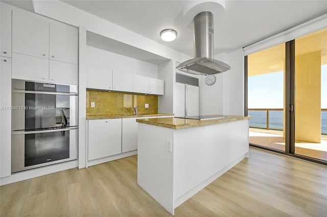 kitchen with expansive windows, island exhaust hood, black electric cooktop, stainless steel double oven, and backsplash