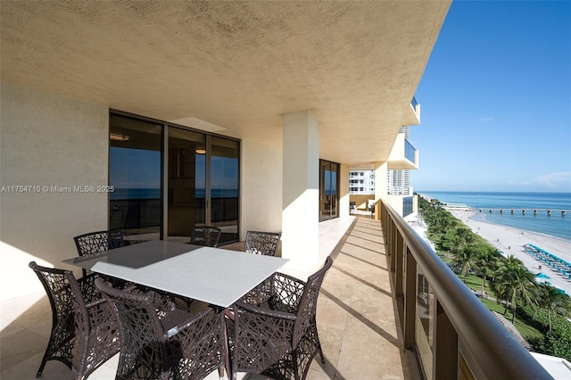 balcony with a beach view, outdoor dining space, and a water view