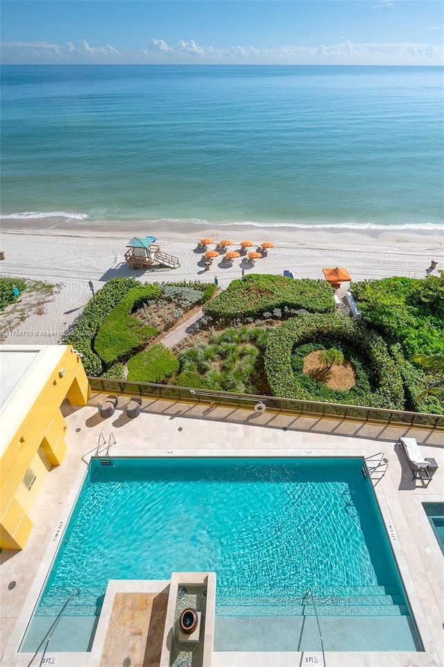 community pool with a patio area, a water view, and a beach view