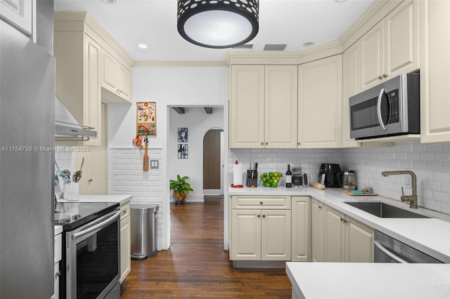 kitchen featuring arched walkways, dark wood-style flooring, stainless steel appliances, backsplash, and a sink