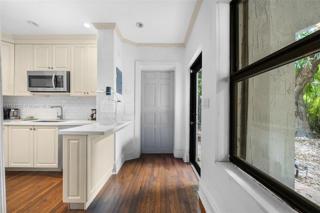 kitchen featuring a peninsula, ornamental molding, decorative backsplash, light countertops, and stainless steel microwave