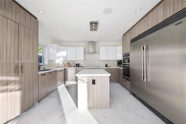 kitchen featuring marble finish floor, appliances with stainless steel finishes, a sink, modern cabinets, and wall chimney exhaust hood