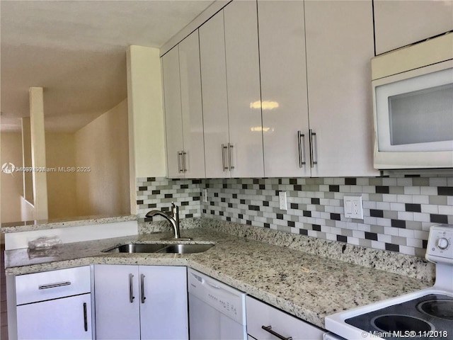 kitchen with light stone counters, tasteful backsplash, white cabinetry, a sink, and white appliances