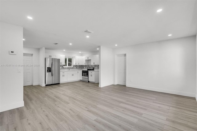 kitchen with stainless steel appliances, white cabinetry, light wood finished floors, and decorative backsplash