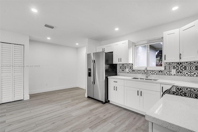 kitchen with a sink, visible vents, backsplash, stainless steel fridge with ice dispenser, and light wood finished floors