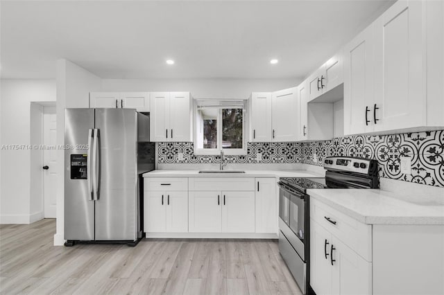 kitchen featuring a sink, white cabinets, appliances with stainless steel finishes, light wood finished floors, and tasteful backsplash