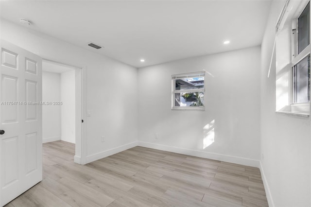 empty room featuring light wood-type flooring, a wealth of natural light, visible vents, and baseboards