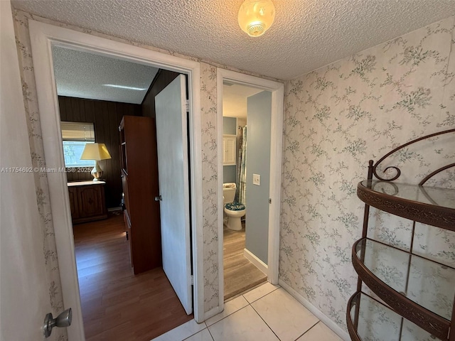 hallway with a textured ceiling, light wood-type flooring, baseboards, and wallpapered walls