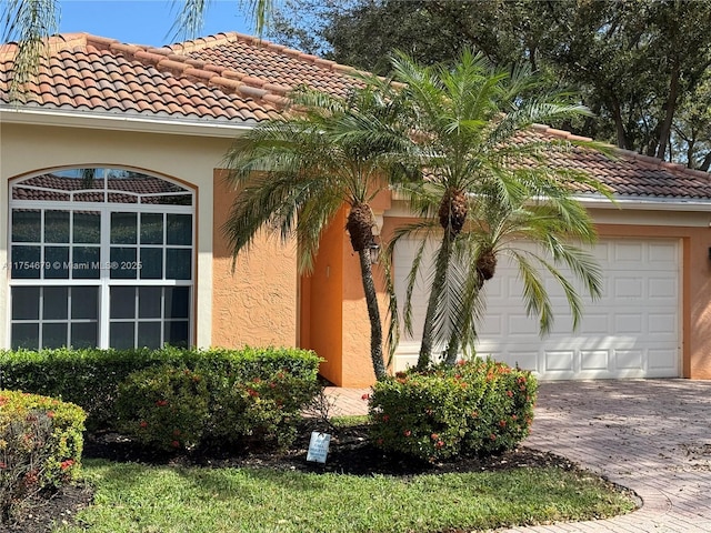 view of side of property featuring a garage, decorative driveway, a tile roof, and stucco siding