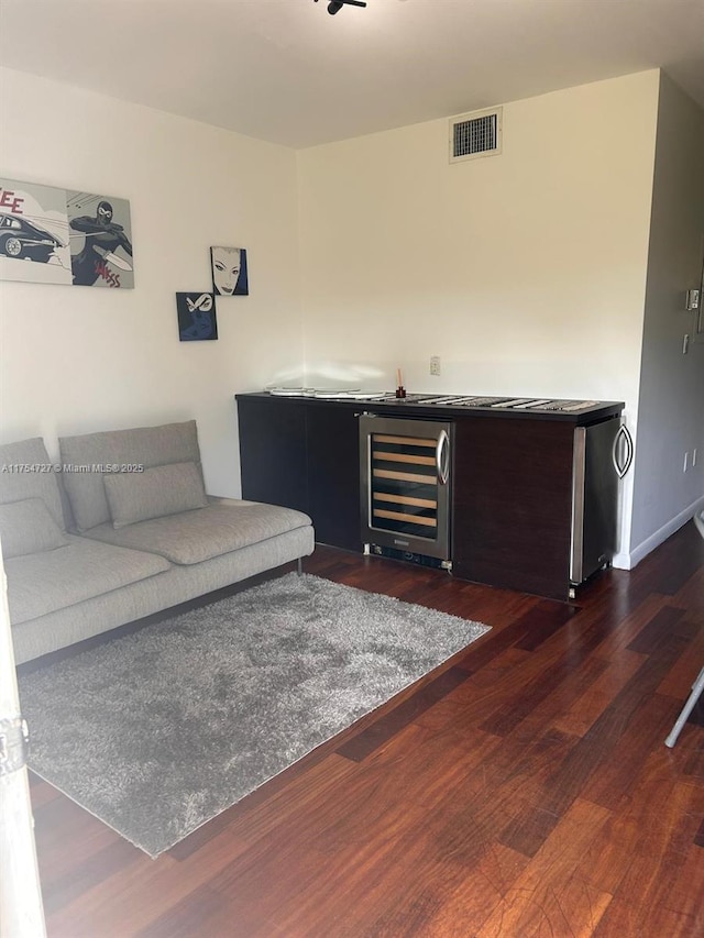 living area featuring visible vents, dark wood finished floors, baseboards, wine cooler, and wet bar