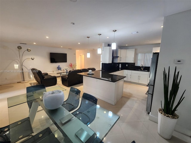 kitchen with white cabinets, open floor plan, wall chimney range hood, freestanding refrigerator, and dark countertops