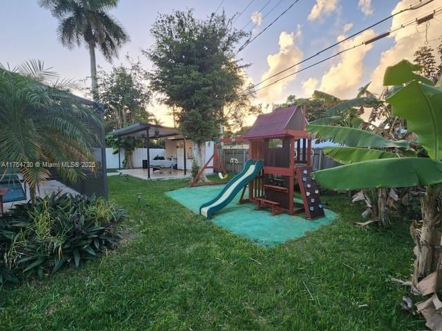 playground at dusk with a patio area, a playground, fence, and a lawn