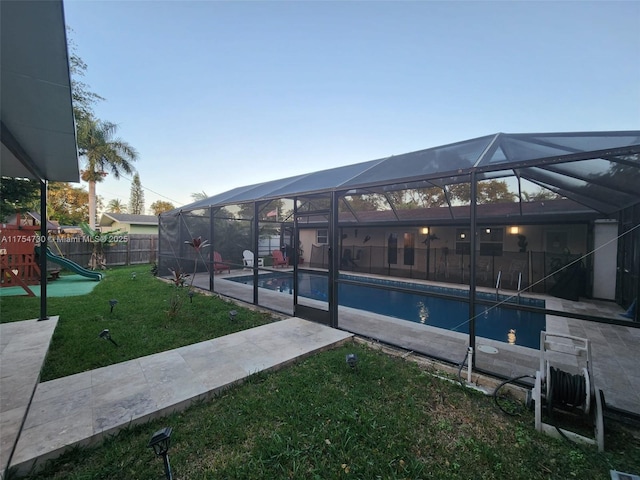 view of swimming pool featuring glass enclosure, a playground, fence, a yard, and a fenced in pool