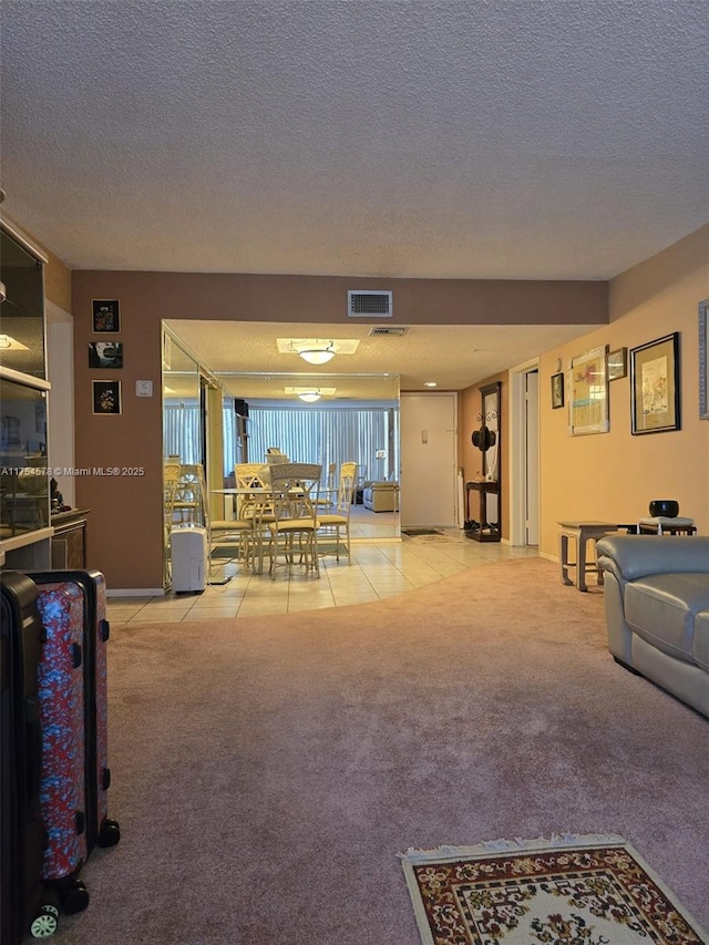 living room featuring light tile patterned floors, visible vents, light carpet, and a textured ceiling