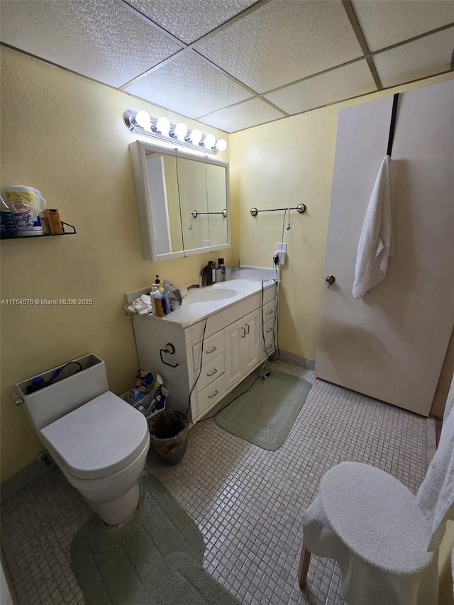 half bathroom featuring tile patterned floors, a drop ceiling, toilet, and vanity