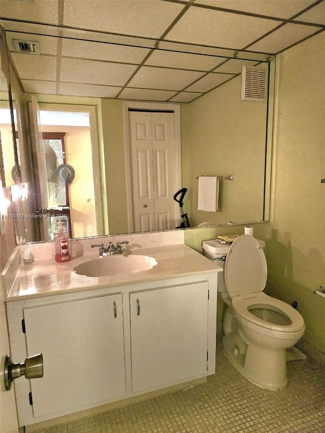 half bathroom featuring a drop ceiling, visible vents, toilet, and vanity