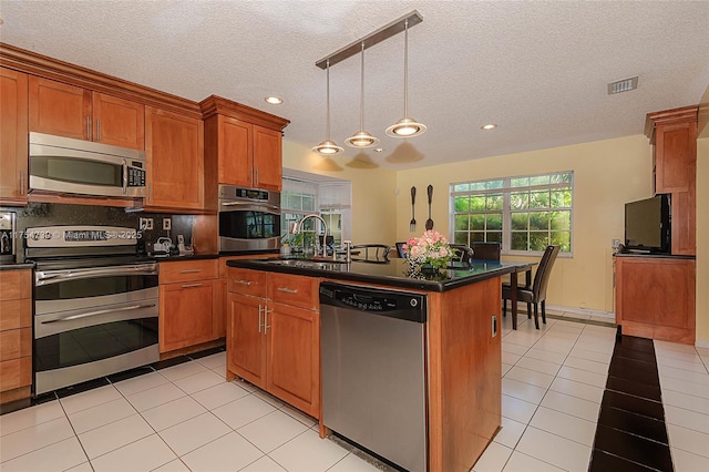 kitchen with visible vents, dark countertops, brown cabinets, a sink, and appliances with stainless steel finishes