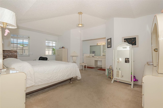 bedroom with ensuite bathroom, vaulted ceiling, a textured ceiling, and light colored carpet