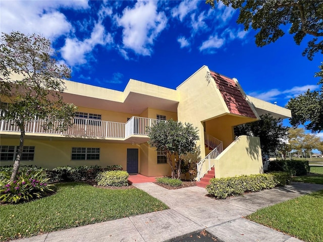 view of front of house featuring stairway, stucco siding, and a front yard