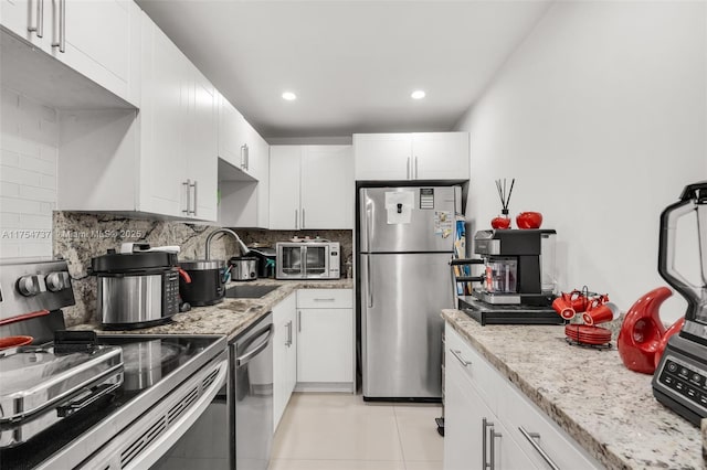 kitchen with white cabinets, stainless steel appliances, decorative backsplash, and light tile patterned flooring