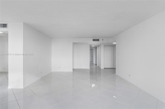 empty room with visible vents, a textured ceiling, and light tile patterned flooring