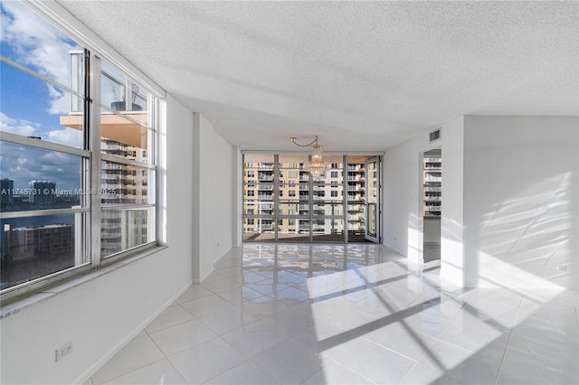 unfurnished room with a city view, visible vents, a textured ceiling, baseboards, and tile patterned floors