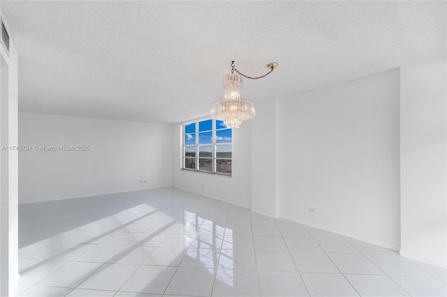 spare room with a textured ceiling, baseboards, a notable chandelier, and light tile patterned flooring