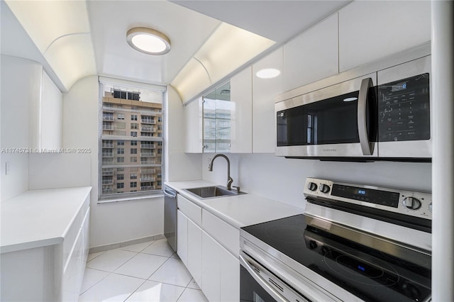 kitchen featuring light tile patterned floors, stainless steel appliances, a sink, and white cabinetry