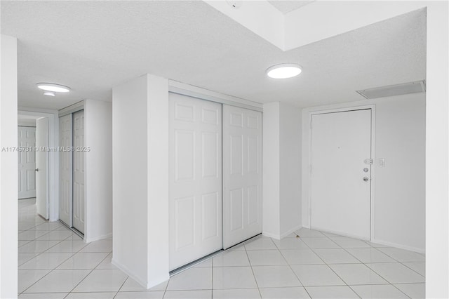 interior space featuring a closet, a textured ceiling, baseboards, and light tile patterned floors