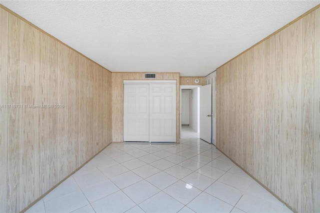 unfurnished bedroom with light tile patterned floors, a closet, visible vents, wood walls, and a textured ceiling