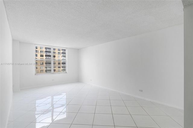 spare room with light tile patterned floors, baseboards, and a textured ceiling