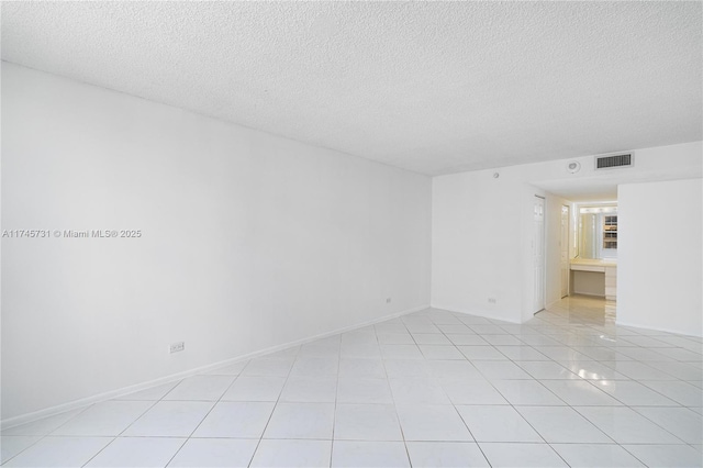 spare room featuring light tile patterned floors, a textured ceiling, visible vents, and baseboards